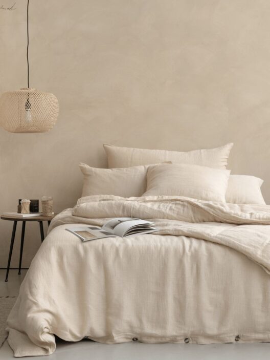 Lit beige avec livre et lampe suspendue.