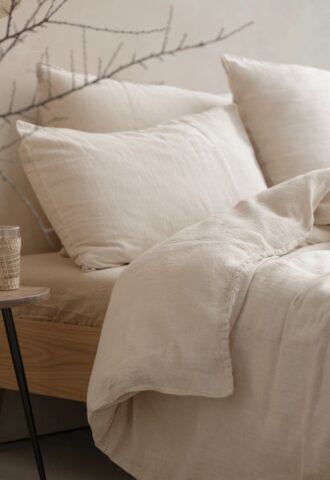 Lit avec draps en lin beige et oreillers.
