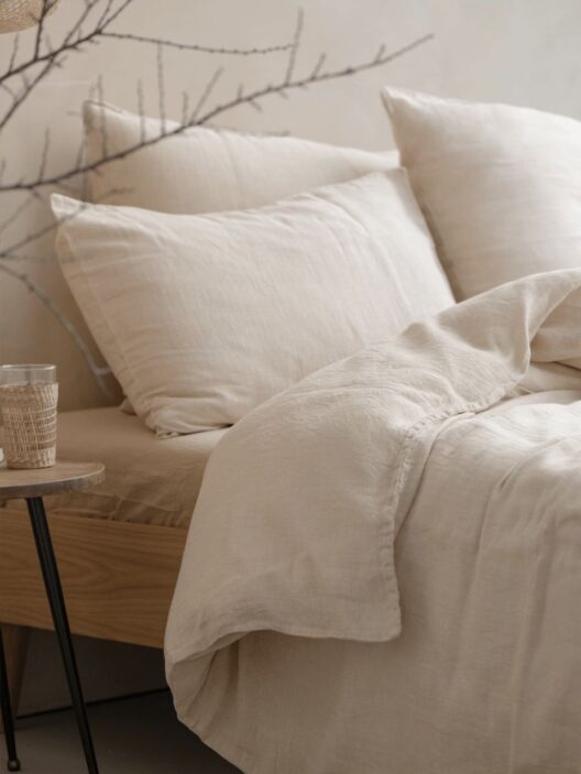 Lit avec draps en lin beige et oreillers.