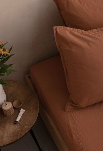 Lit brun avec table de chevet et fleurs.