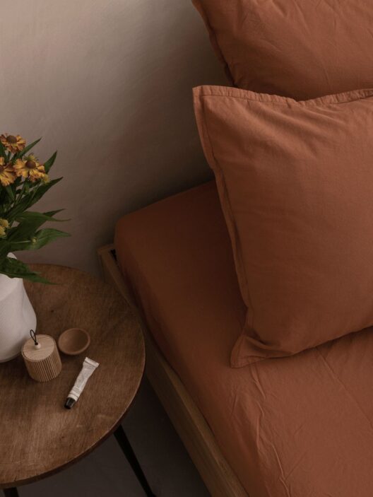 Lit brun avec table de chevet et fleurs.