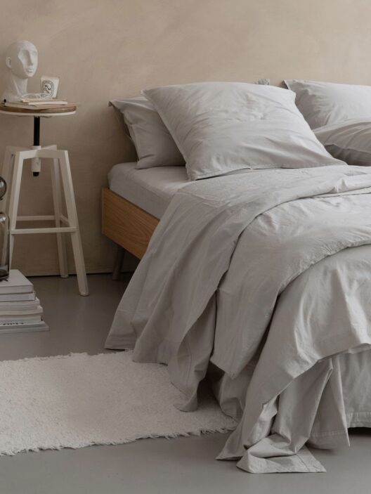 Lit avec draps gris et table de chevet.