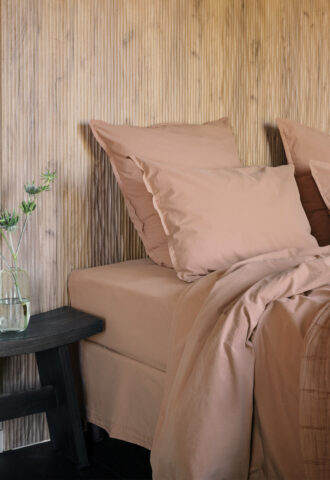 Lit avec draps roses et vase sur table