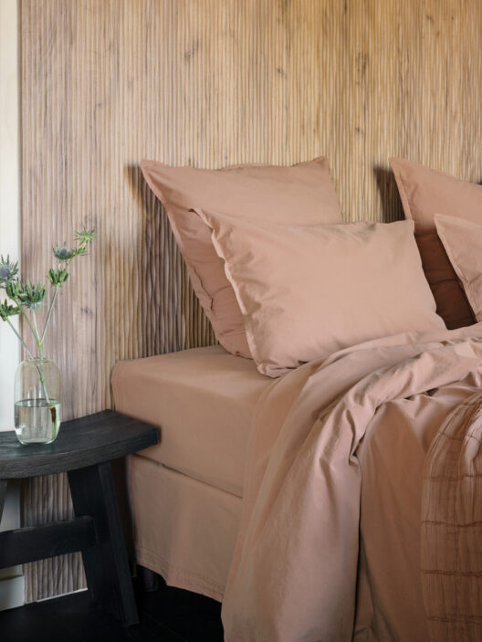 Lit avec draps roses et vase sur table