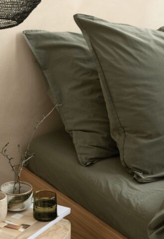 Lit avec draps verts et accessoires décoratifs.