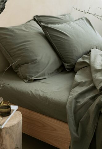 Lit avec draps verts et table de chevet.