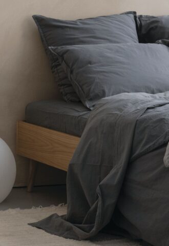 Lit avec draps gris sombre et coussins.