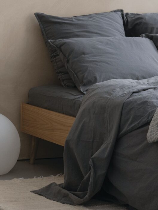 Lit avec draps gris sombre et coussins.