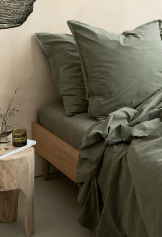 Lit avec draps verts, table en bois.