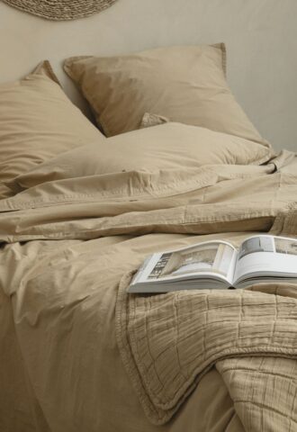 Lit beige avec livre ouvert sur le duvet.