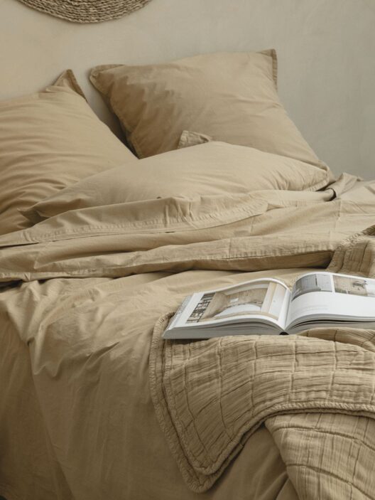 Lit beige avec livre ouvert sur le duvet.