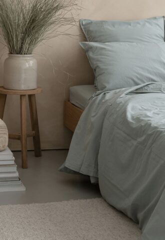 Lit avec draps bleus et vase déco.