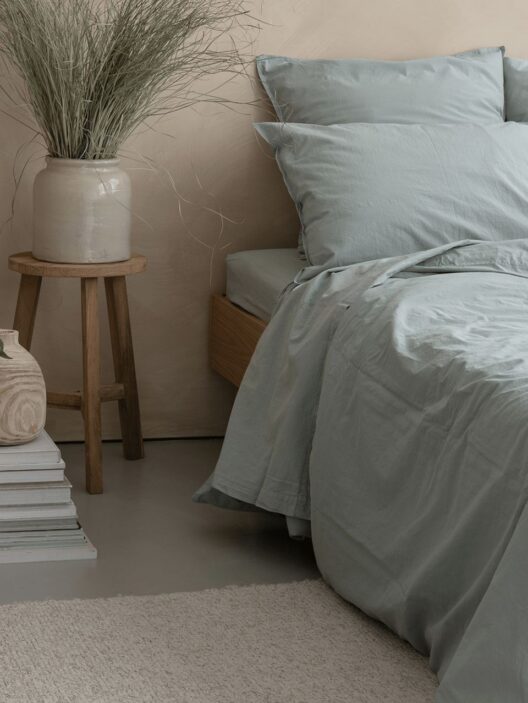 Lit avec draps bleus et vase déco.