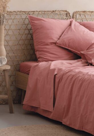 Lit avec draps roses et décoration naturelle.