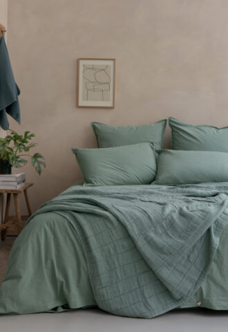 Lit avec draps verts et décoration minimaliste.