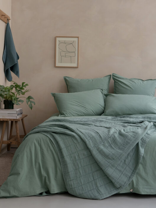 Lit avec draps verts et décoration minimaliste.