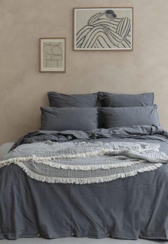 Lit avec draps gris et tableaux au mur.