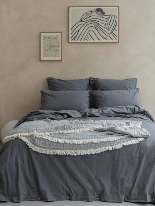 Lit avec draps gris et tableaux au mur.