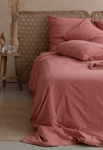 Lit avec draps roses et décoration en rotin.