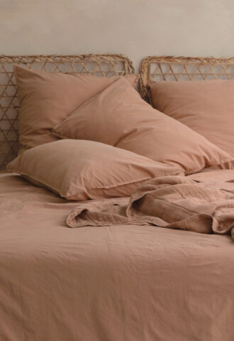 Lit avec draps beiges et oreillers assortis.