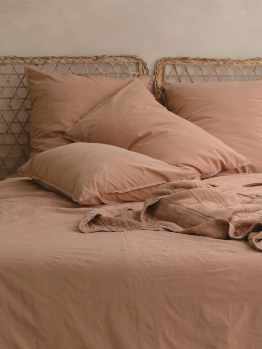 Lit avec draps beiges et oreillers assortis.