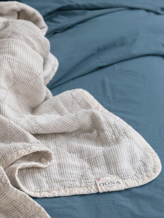 Couverture rayée blanche sur drap bleu.