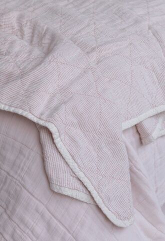 Couverture rose avec rayures blanches sur un lit.