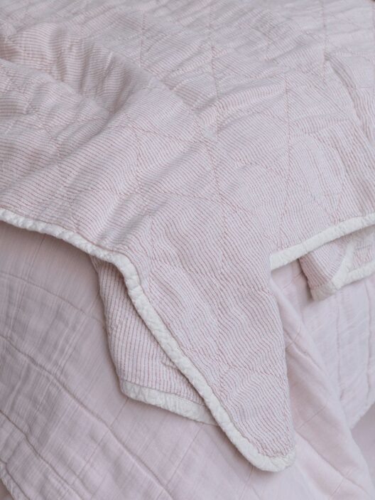 Couverture rose avec rayures blanches sur un lit.