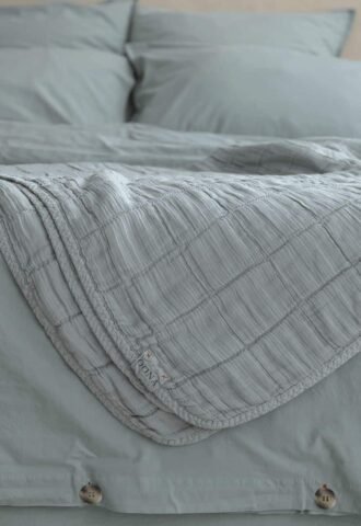 Lit avec couverture grise et oreillers assortis.