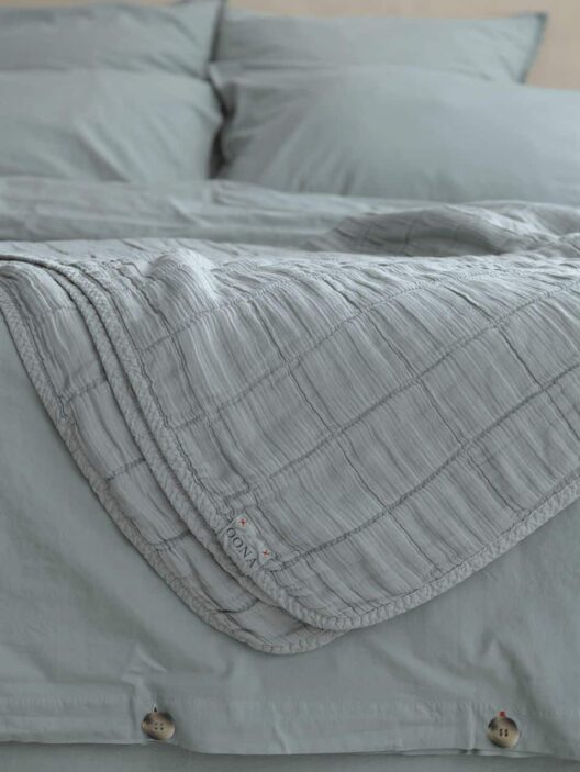 Lit avec couverture grise et oreillers assortis.