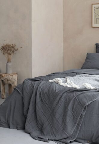 Lit avec couvre-lit gris dans chambre minimaliste.