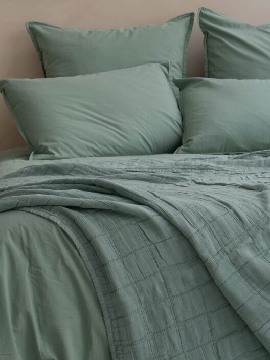 Lit avec draps verts et coussins assortis.