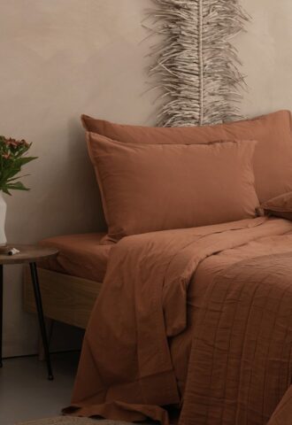 Lit avec draps marron et plante verte.