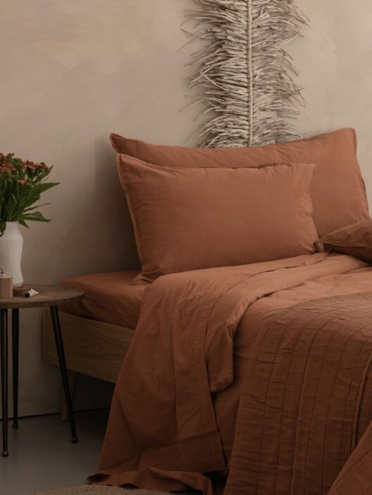 Lit avec draps marron et plante verte.