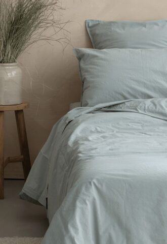 Lit avec draps bleus et vase décoratif.