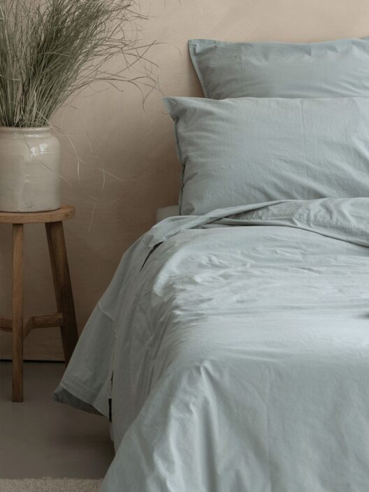 Lit avec draps bleus et vase décoratif.