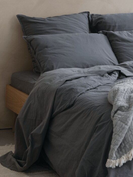 Lit avec draps et oreillers gris.