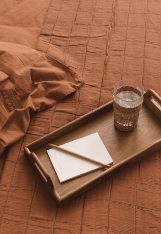 Plateau avec verre et papier sur lit orange.