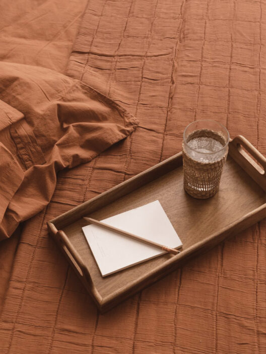 Plateau avec verre et papier sur lit orange.