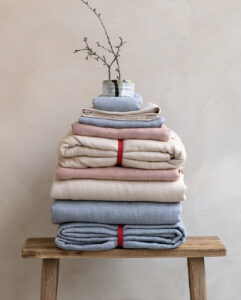 Tissus pliés avec vase sur tabouret en bois.