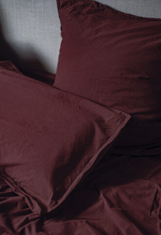 Linge de lit en coton bordeaux sur un lit.