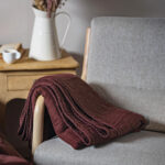 Couverture prune sur fauteuil gris avec vase.