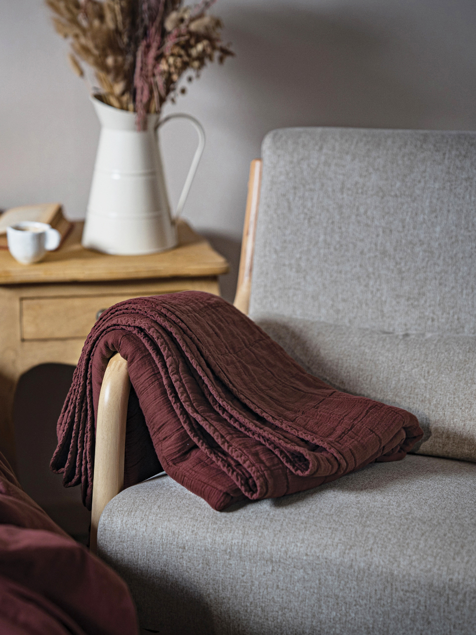 Couverture prune sur fauteuil gris avec vase.