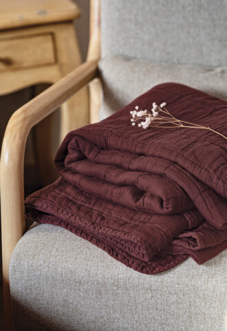 Plaid bordeaux plié sur fauteuil beige.