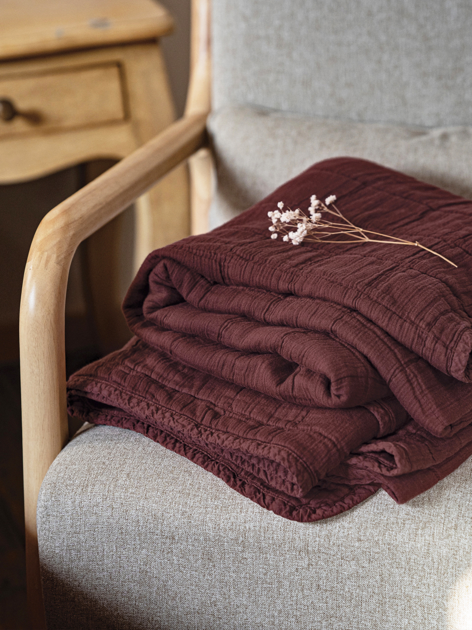 Plaid bordeaux plié sur fauteuil beige.