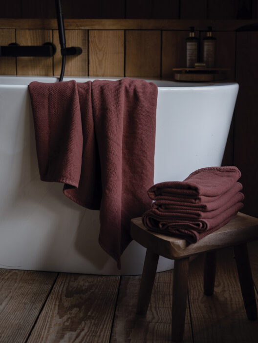 Serviettes bordeaux sur baignoire blanche et tabouret.