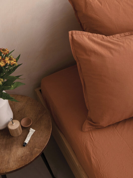 Lit aux draps terracotta et table de chevet